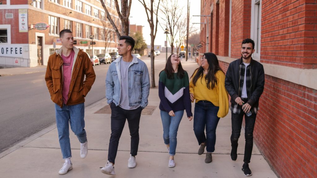 Five diverse students walk along an off-campus downtown sidewalk.